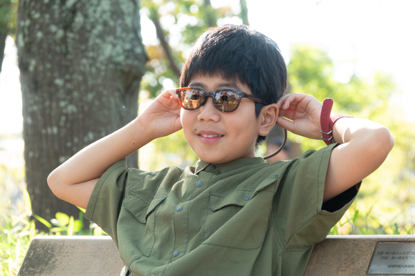 キッズ向けサングラスsolasidoを装着して笑っている男の子が公園のベンチで座っている