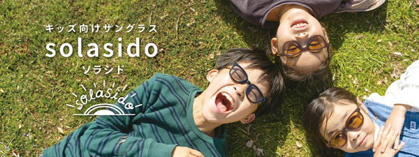 男の子と女の子の子供がキッズサングラスsolasidoをつけて芝生に寝そべって笑っている