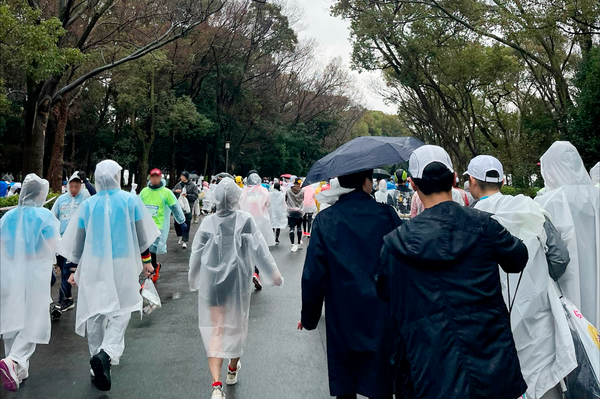雨天のマラソン大会に参加するランナーたち。ポンチョや傘で雨をしのぎながらスタート地点へ向かう様子。